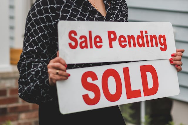A lady holding a 'sale pending' and 'sold' sign.