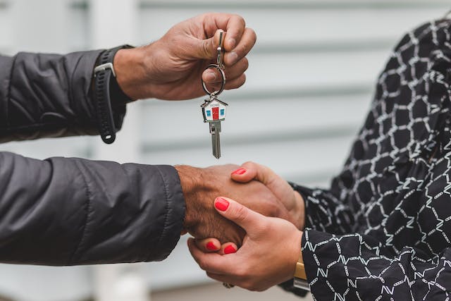 A pair of hands handing over a house key to another pair of hands.
