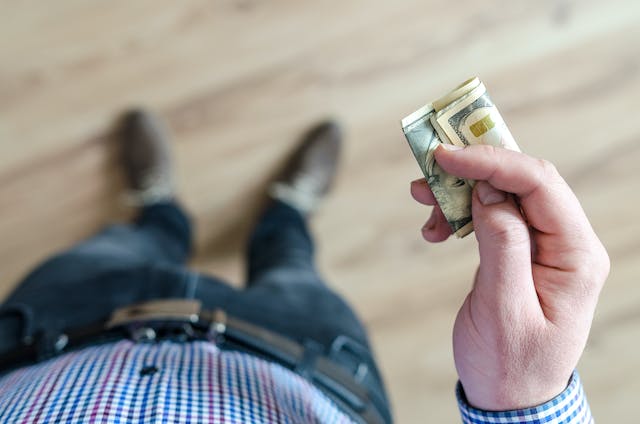A man standing holding out a roll of cash.