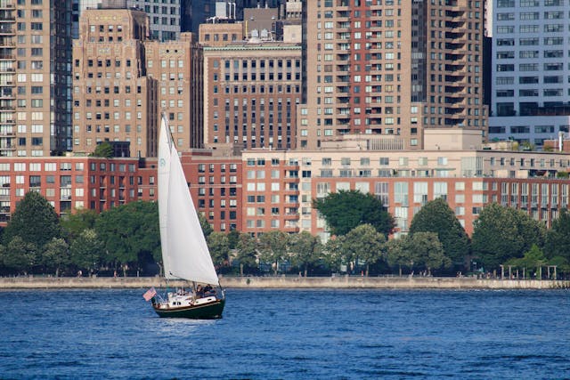 White sail boat on water near city buildings.