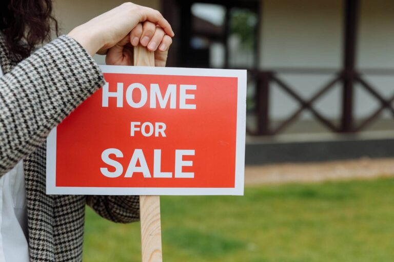 A realtor holding a sign "Home For Sale" in front of a home.
