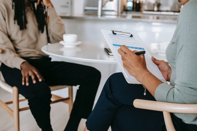 A person with a clipboard sitting interviewing another person.